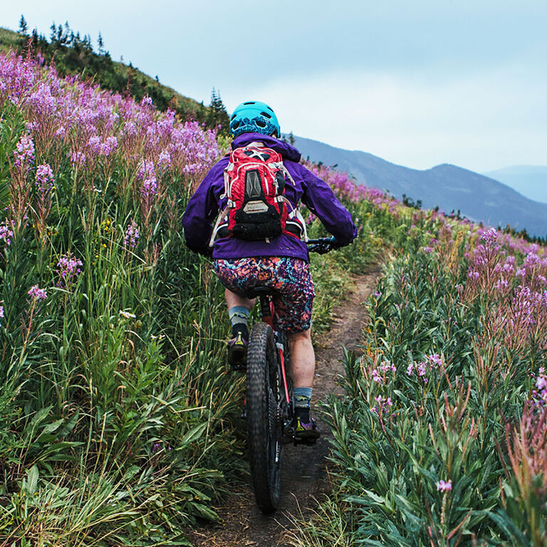 man riding bike on single track through wild flowers